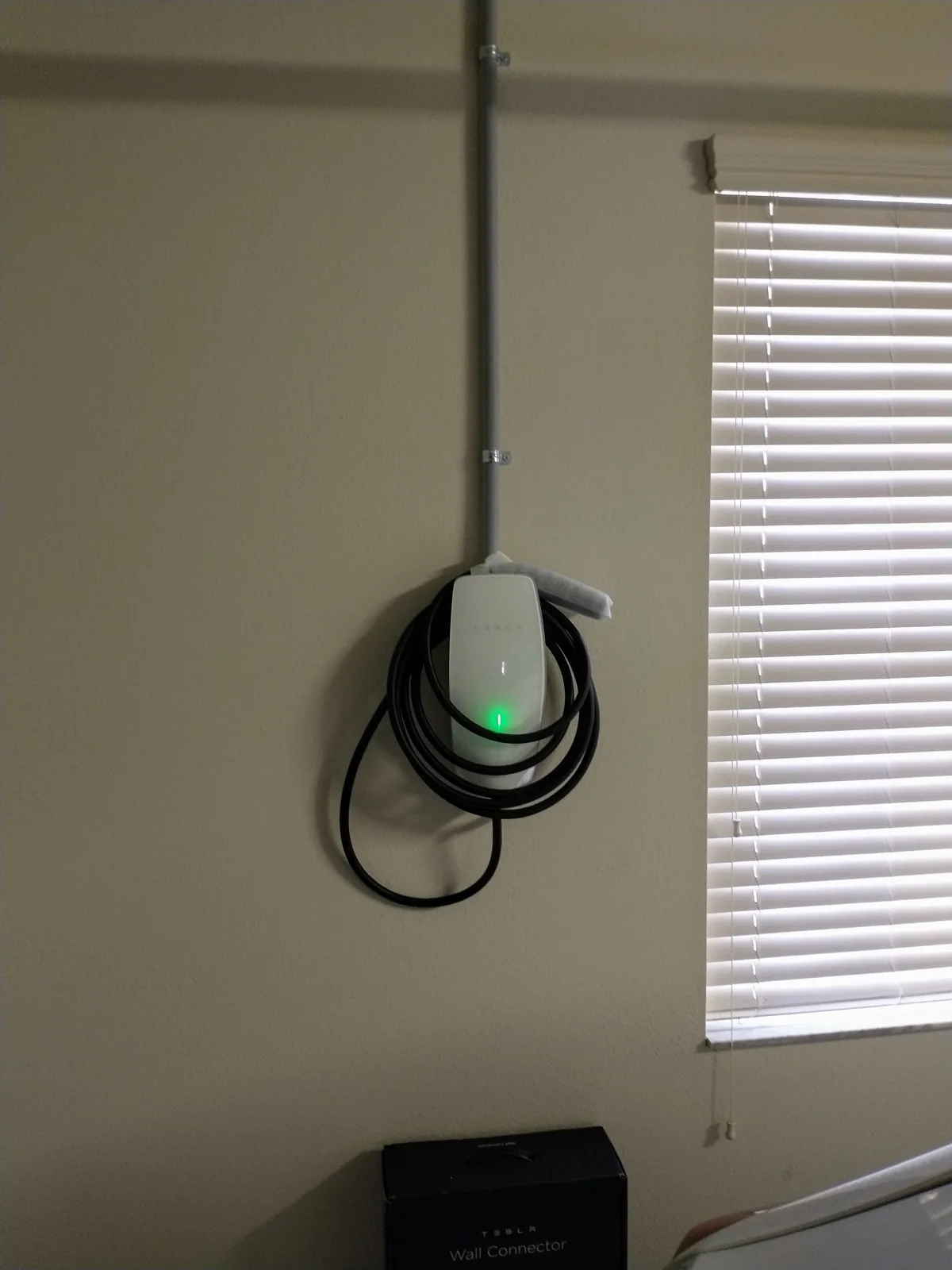 Wall-mounted EV charger in a garage with the charging cable coiled beside it