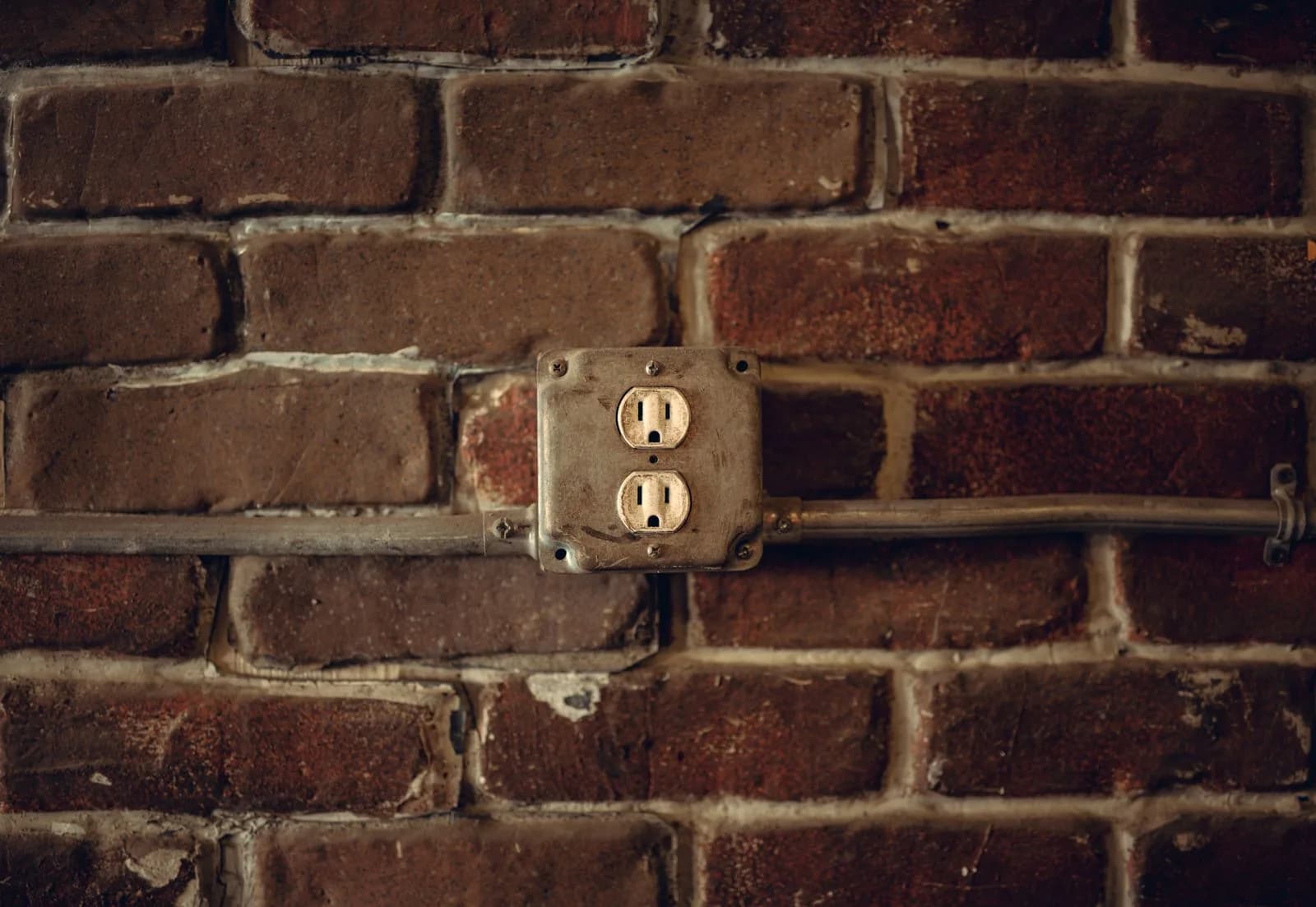 Older two-prong duplex outlet mounted in a metal box, the type of outlet homeowners often ask to have updated