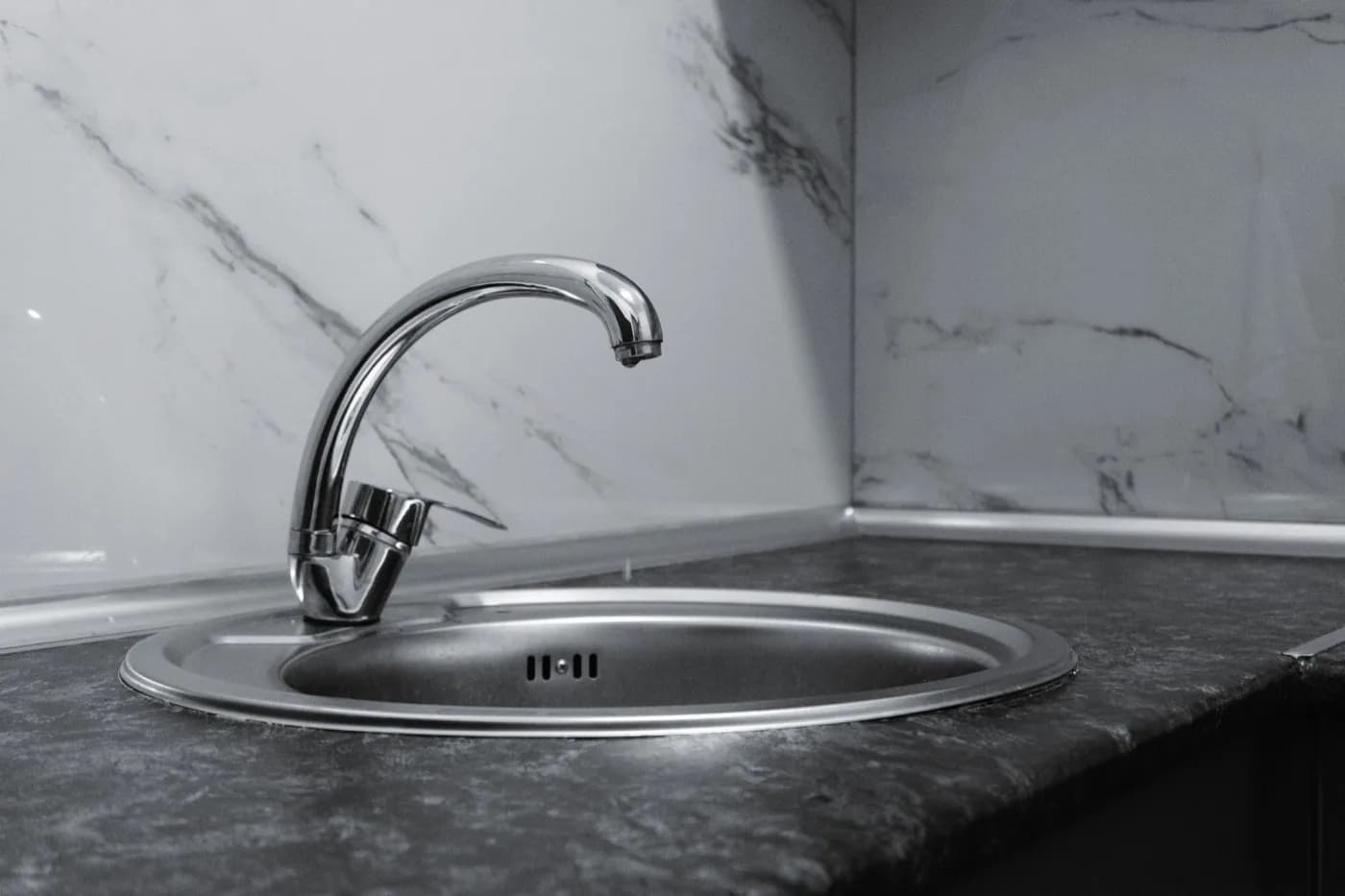 Stainless steel kitchen faucet installed against a marble backsplash